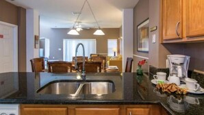 A modern kitchen with a black granite countertop, stainless steel sink, wooden cabinets, and a dining area with a table and chairs. - Encantada Resort (Kissimmee)