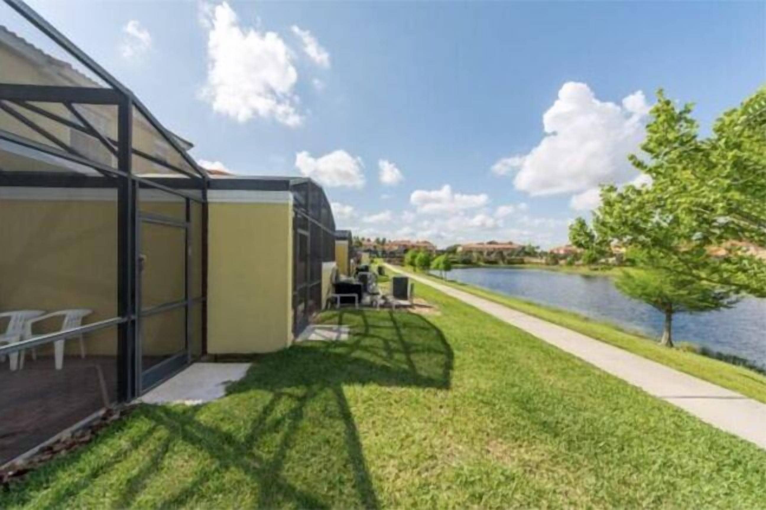 A modern building with a glass facade, a patio with outdoor furniture, and a view of a lake.