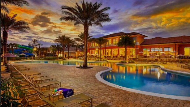 A resort pool area with lounge chairs, palm trees, and a building with multiple windows. - Encantada Resort (Kissimmee)