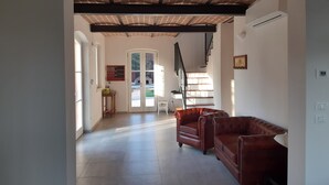 A spacious living area with a high ceiling, a staircase, and a door leading to an outdoor area. - B&B Santa Maria di Lorgana (Minerbio)