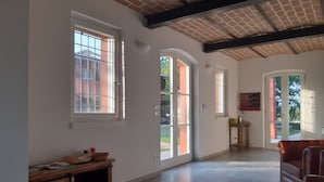 A spacious room with large windows, a wooden cabinet, and a leather sofa. - B&B Santa Maria di Lorgana (Minerbio)