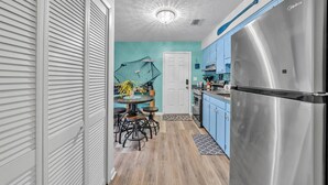 Una cocina con pared verde azulado, un refrigerador de acero inoxidable y un comedor con mesa y sillas redondas.