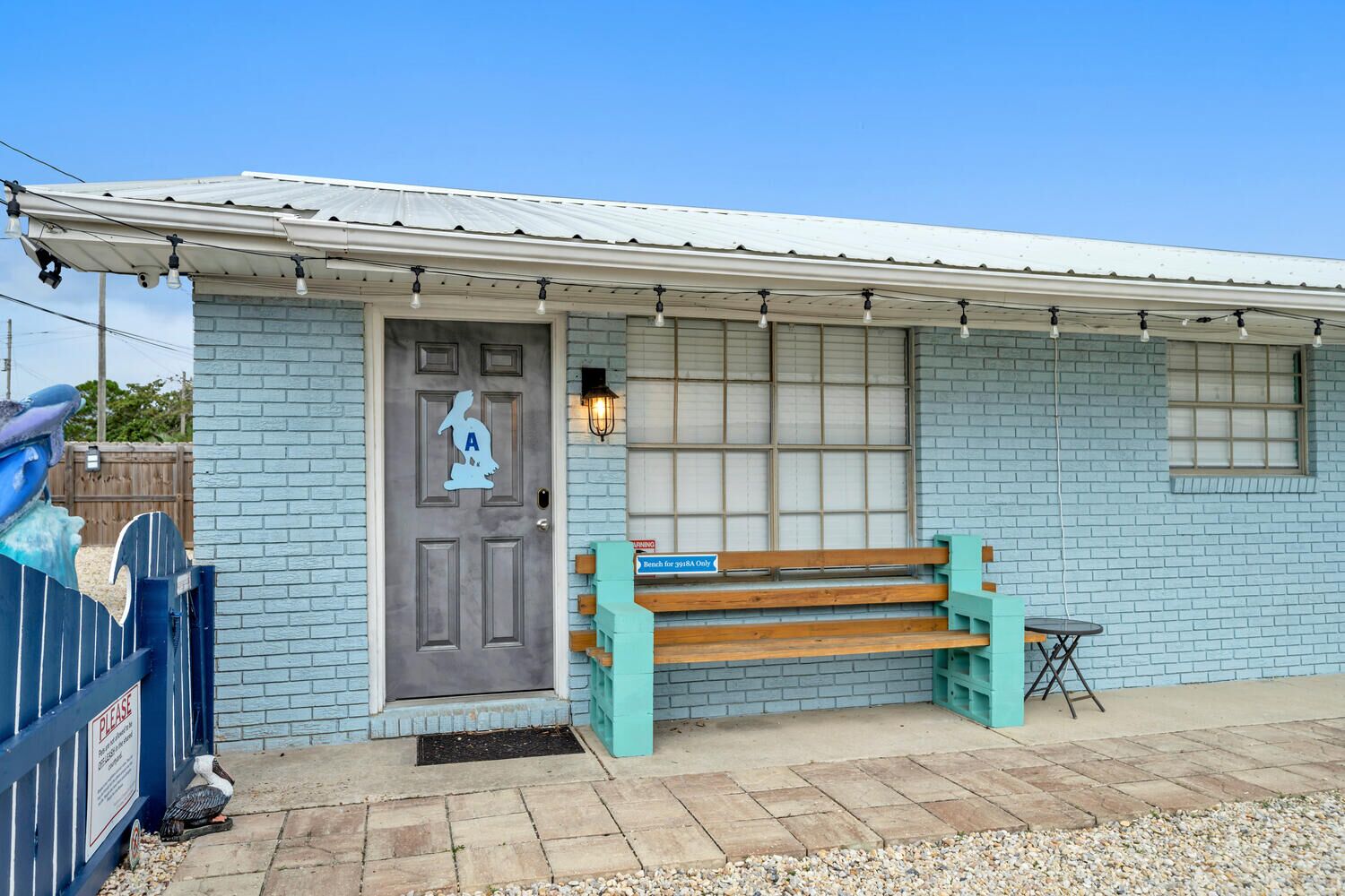 Um edifício com porta cinza, um banco e uma pequena mesa na parte externa.