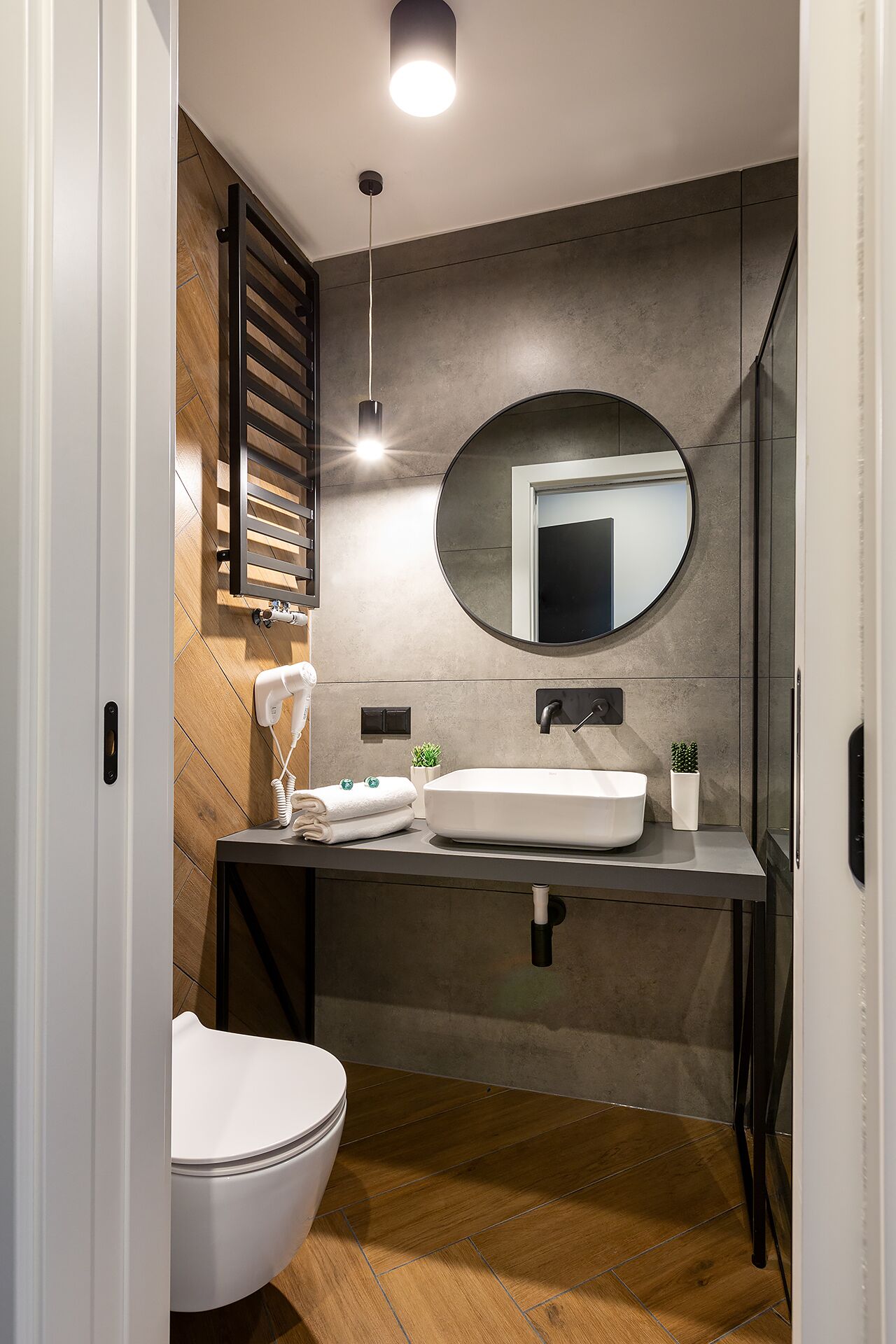 Un baño moderno con inodoro blanco, un espejo redondo grande y un lavamanos blanco.