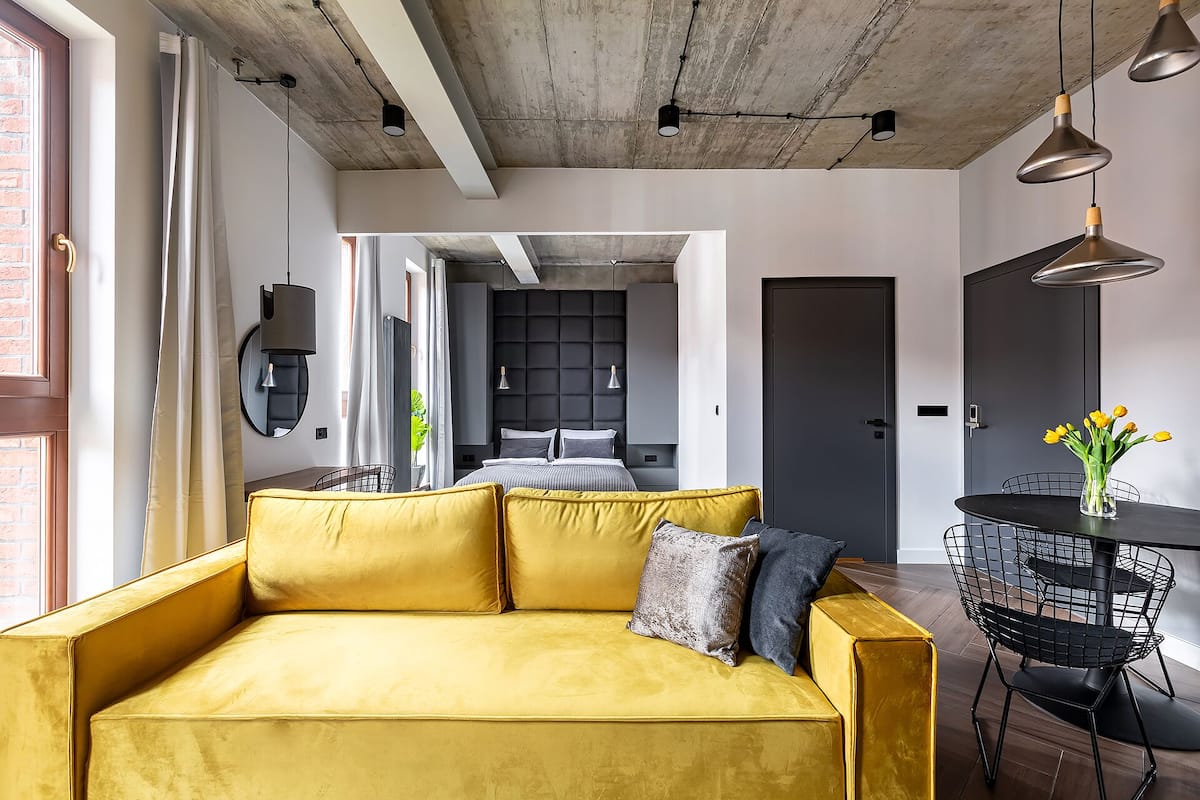 Un espacio habitable moderno con un sofá amarillo, una mesa de comedor con sillas y una zona de cocina al fondo.