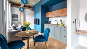 A modern kitchen with blue walls, wooden cabinets, and a round dining table with blue chairs.