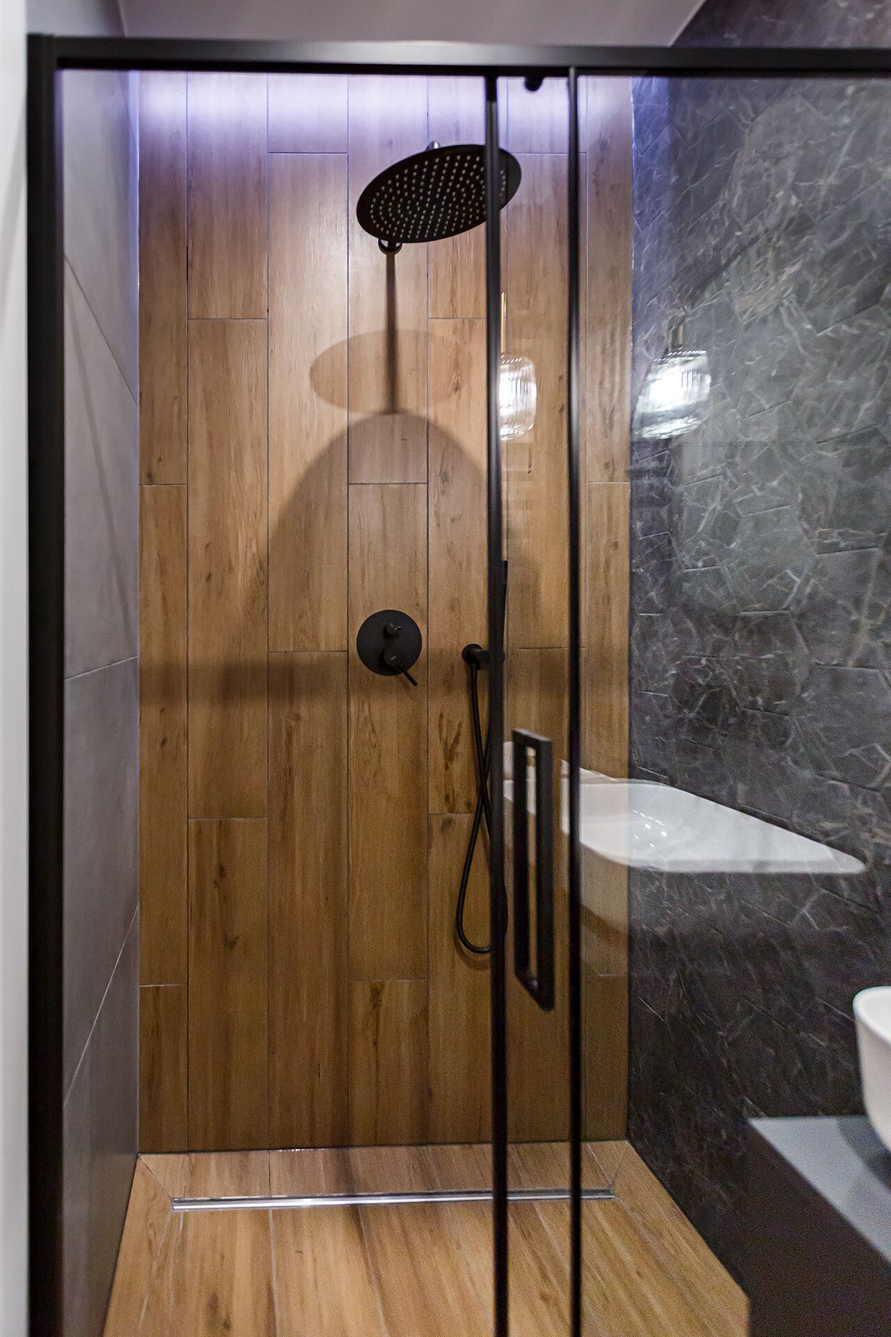 Eine moderne Duschkabine mit Wandverkleidung aus Holz, einer Glastür und einer Marmor-Spritzschutzwand.