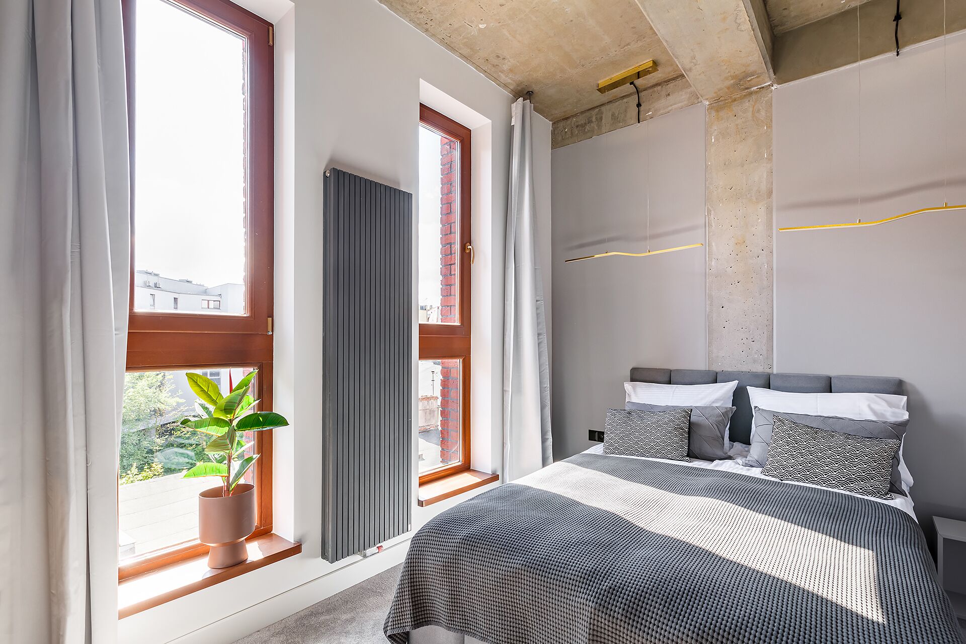 A modern bedroom with a large bed, a potted plant, and a view of the city.