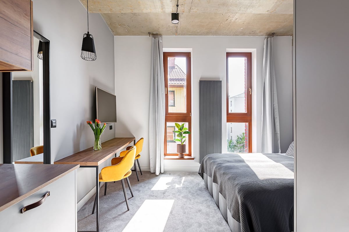 Un dormitorio moderno con una cama, un escritorio con silla, un televisor y una ventana con cortinas.