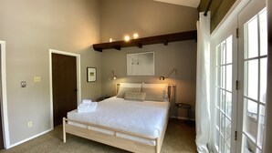 Un dormitorio con cama, lámparas de noche, una puerta y una ventana.