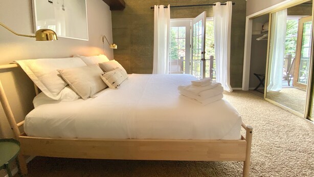 Un dormitorio con una cama grande, una mesita de noche, una lámpara de pared y vistas al exterior a través de una puerta de cristal.