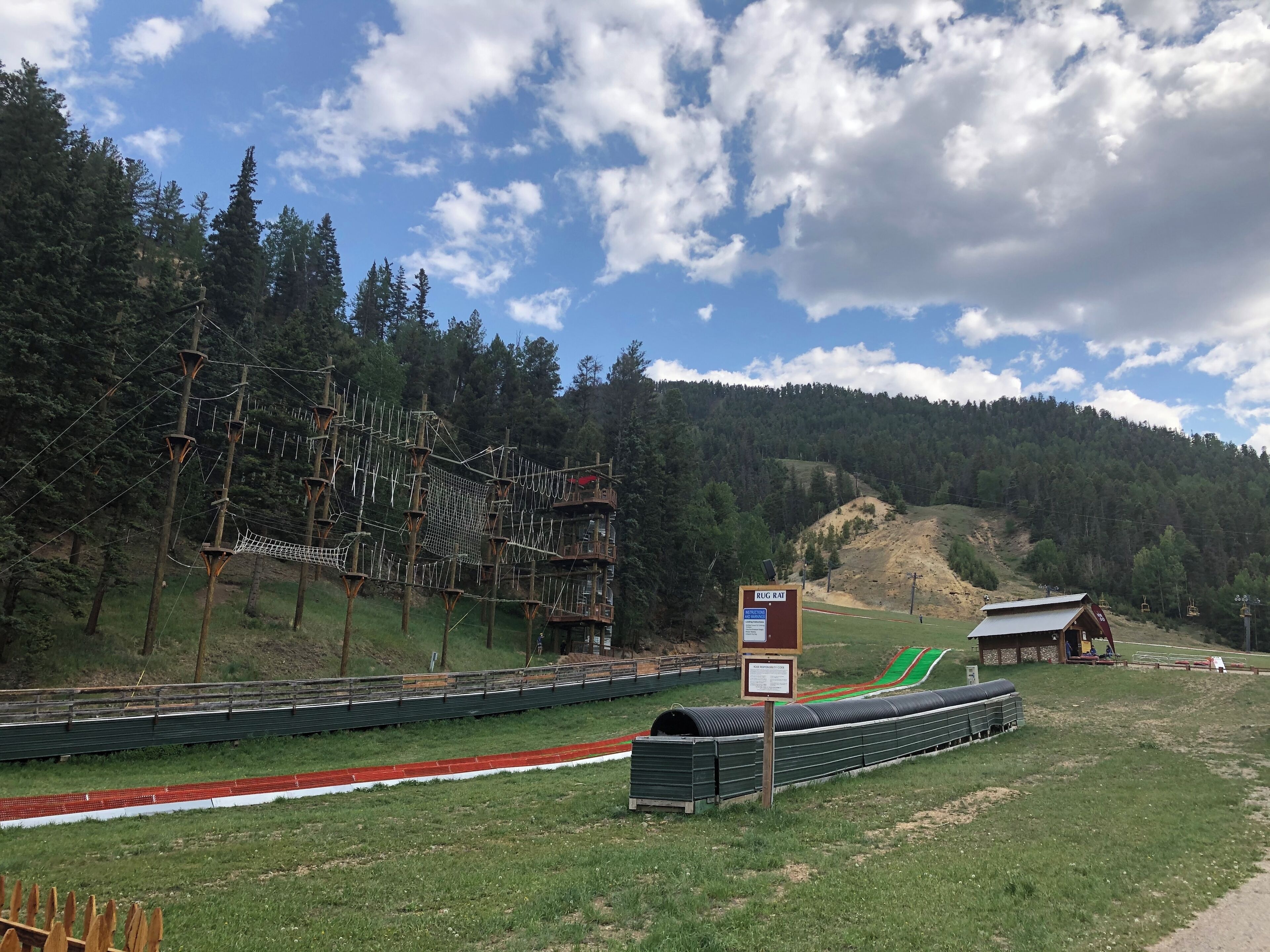 A rope bridge, a wooden structure, and a signboard in a mountainous area.