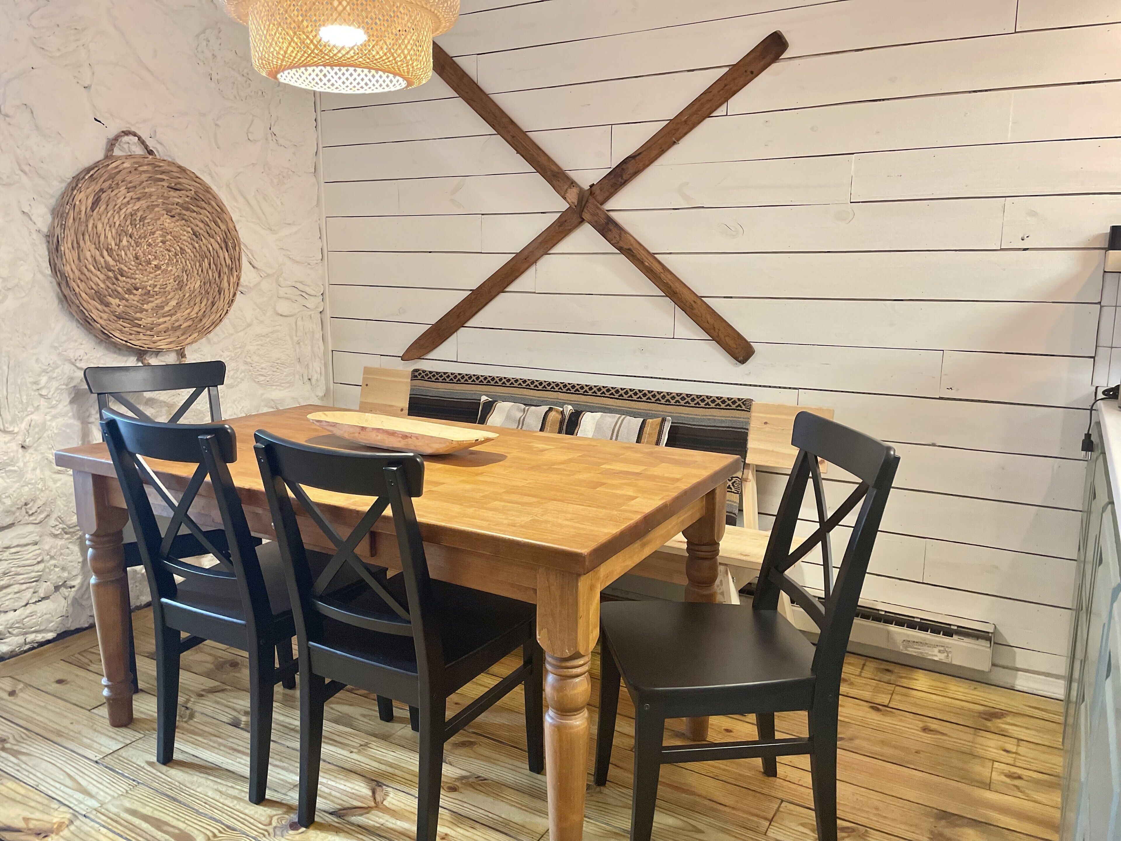 A dining area with a wooden table and black chairs, a woven wall hanging, and a wooden beam on the wall.