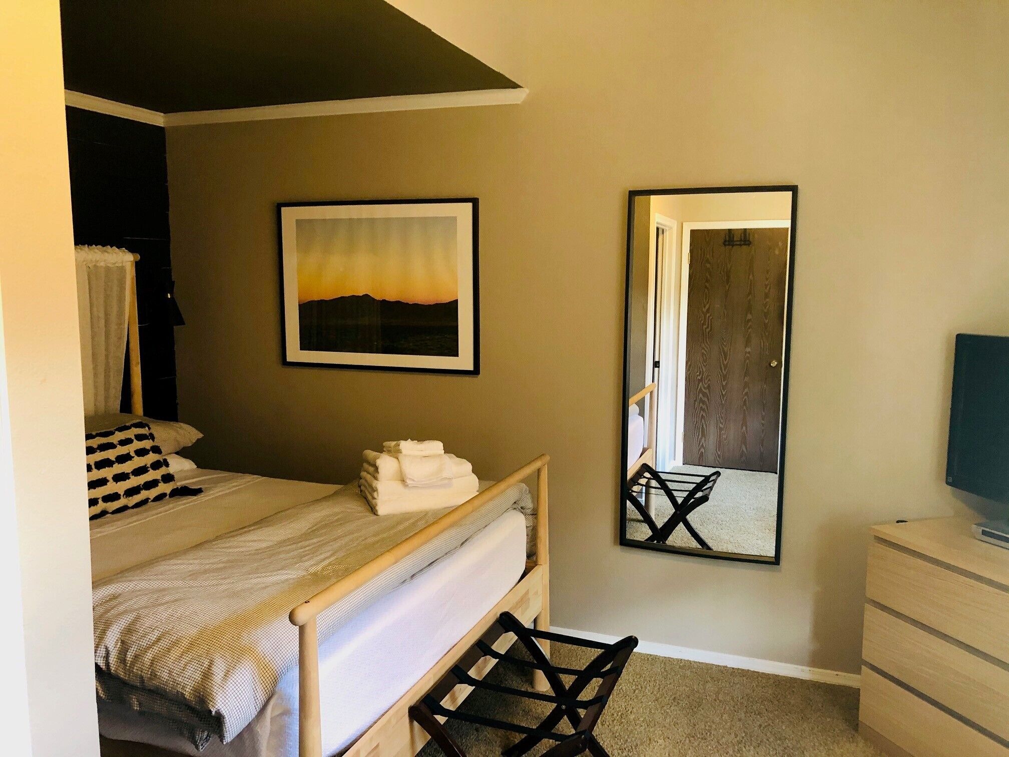 A bedroom with a bed, a bedside table, a dresser, a mirror, and a framed picture on the wall.