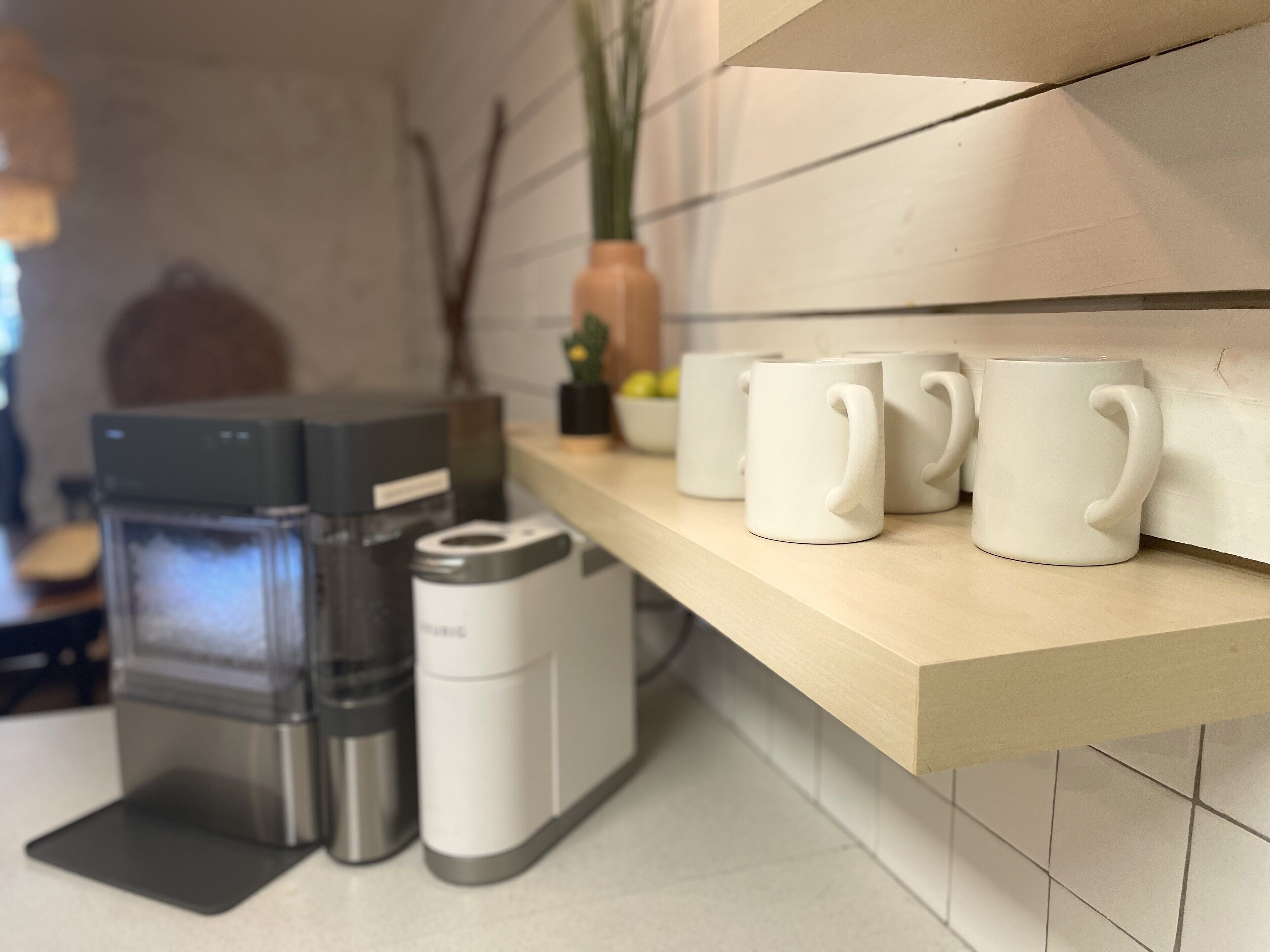A kitchen counter with a coffee maker, a toaster, and three white mugs.