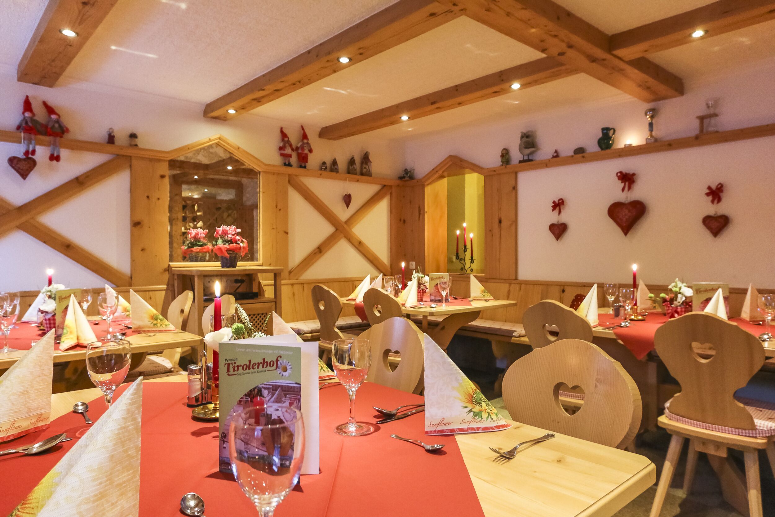 A restaurant with wooden beams, heart-shaped decorations, and tables set with red tablecloths and wine glasses.