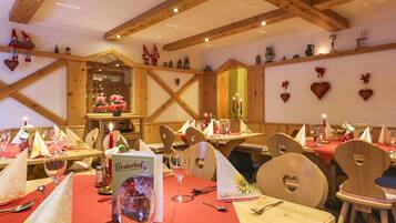 A restaurant with wooden beams, heart-shaped decorations, and tables set with red tablecloths and wine glasses.