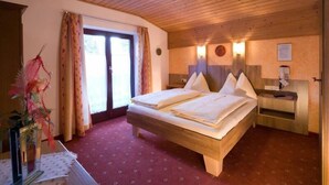A room with a wooden ceiling, a bed with white linens, a nightstand, and a vase with flowers. - Tirolerhof (St. Ulrich Am Pillersee)
