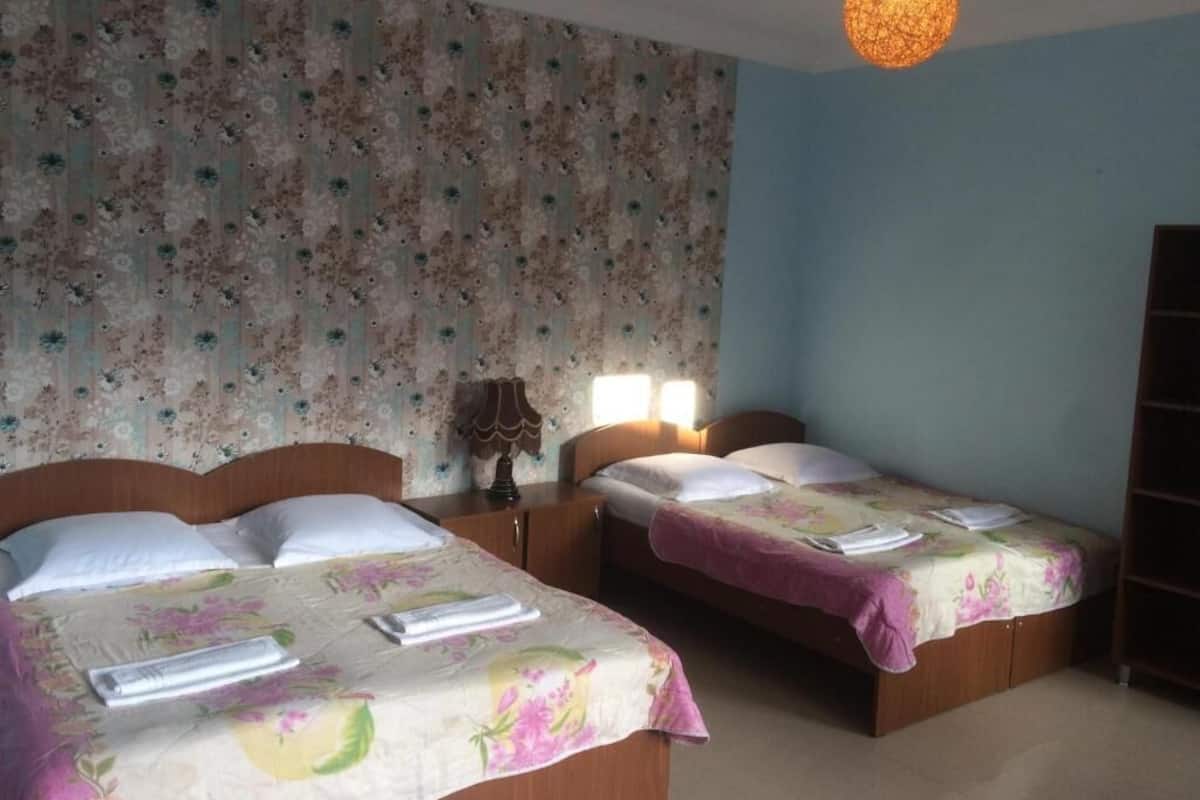 A hotel room with two beds, floral wallpaper, a wooden headboard, bedside lamps, and a hanging light fixture.