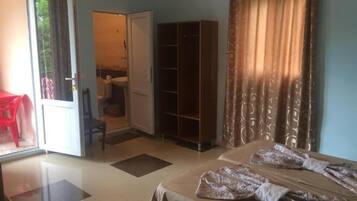 Una habitación de hotel con cama, armario, puerta que da a un balcón y una silla roja.