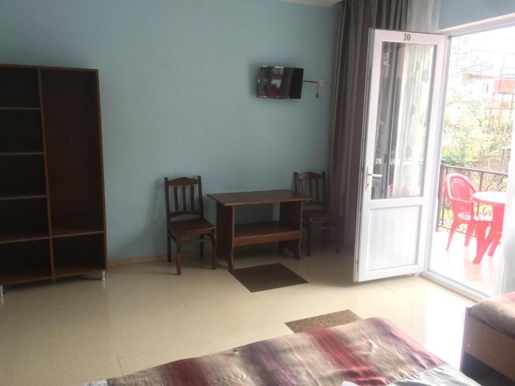 Een kamer met een grote inbouwkast, een aan de muur bevestigde televisie, een eettafel met stoelen en een schuifdeur van glas die leidt naar een buitengebied met een rode stoel.