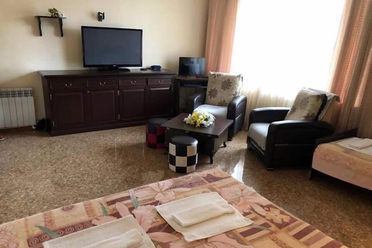 A living room with a sofa, armchairs, a coffee table, a TV, and a radiator.