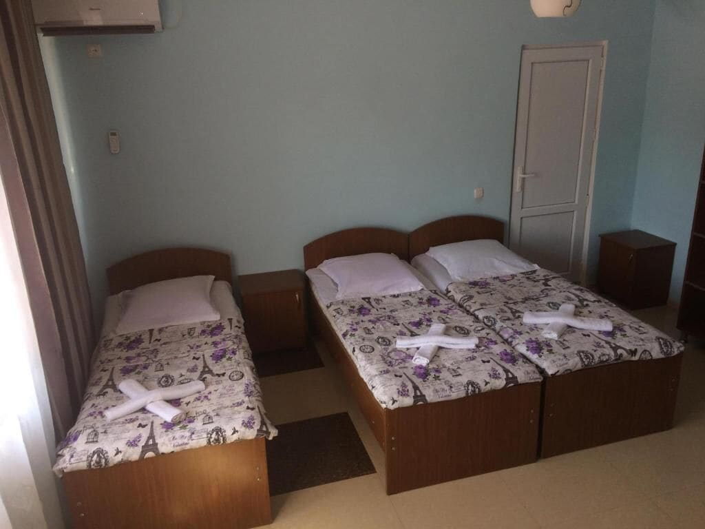 Una habitación con dos camas de madera, cada una con una colcha estampada con motivos florales y almohadas blancas. Hay mesitas de noche y un armario en la habitación.