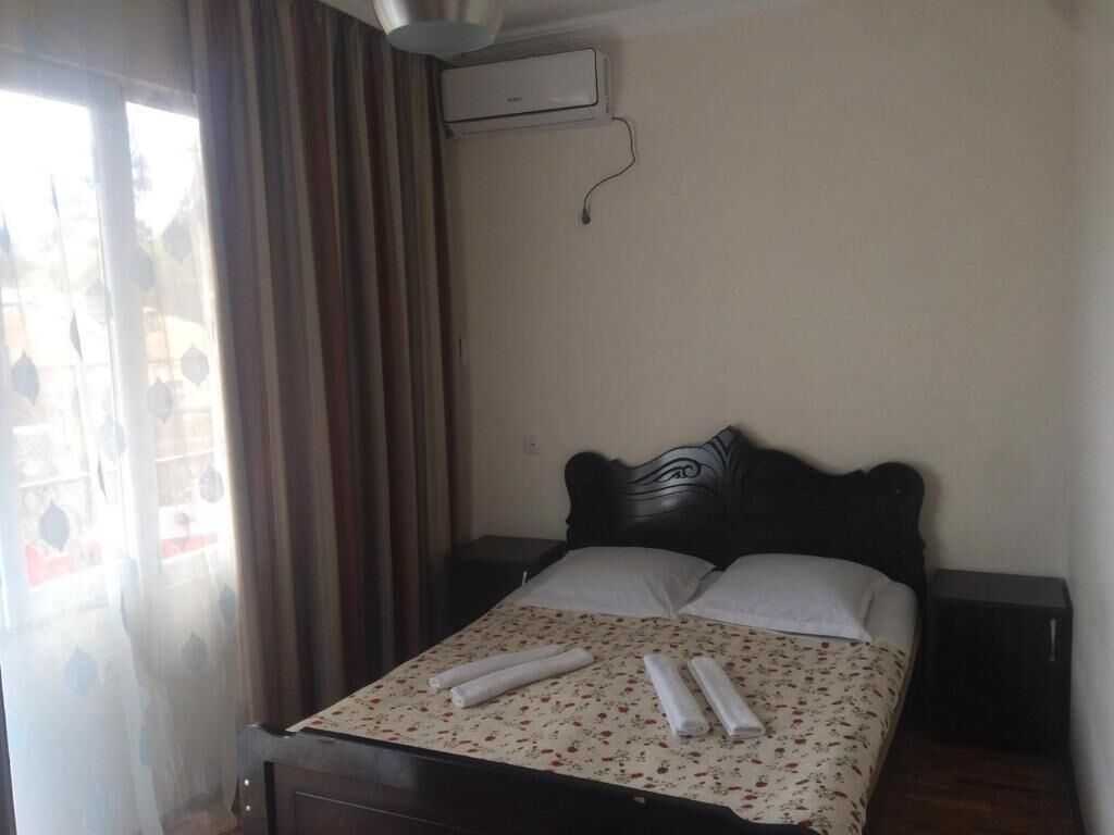 A neatly made bed with a floral bedspread and rolled towels, a dark headboard, and an air conditioning unit on the wall.