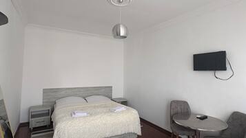 A hotel room with a bed, bedside tables, a TV mounted on the wall, a small round table, and a chair.