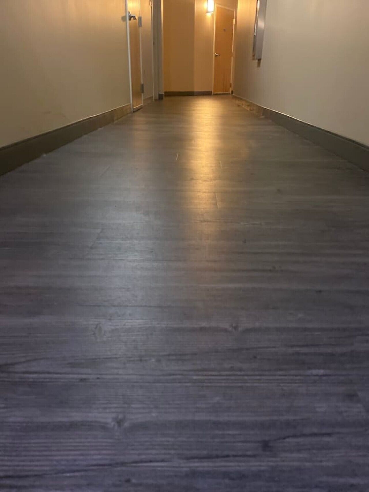 A hallway with a wooden floor, doors on the left, and a light at the end.