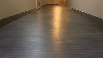 A hallway with a wooden floor, doors on the left, and a light at the end.
