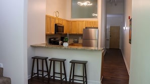 A kitchen with wooden cabinets, a stainless steel refrigerator, a microwave, and a sink. There are three bar stools and a potted plant on the counter. - 360° TERRACE VIEW KING BEDS SELF CHECK-IN WIFI W/D (Indianapolis)