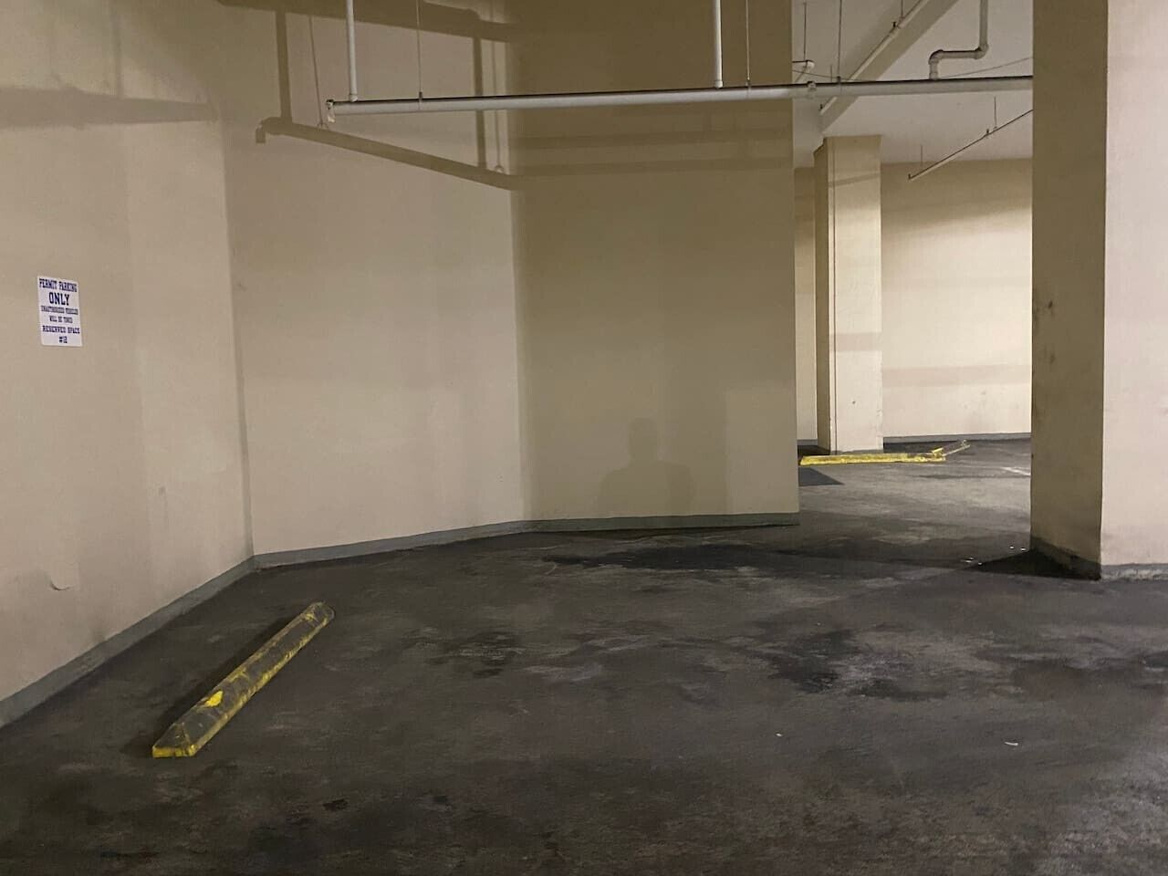 A parking garage with concrete floors and walls, a yellow caution tape on the ground, and a sign on the wall.