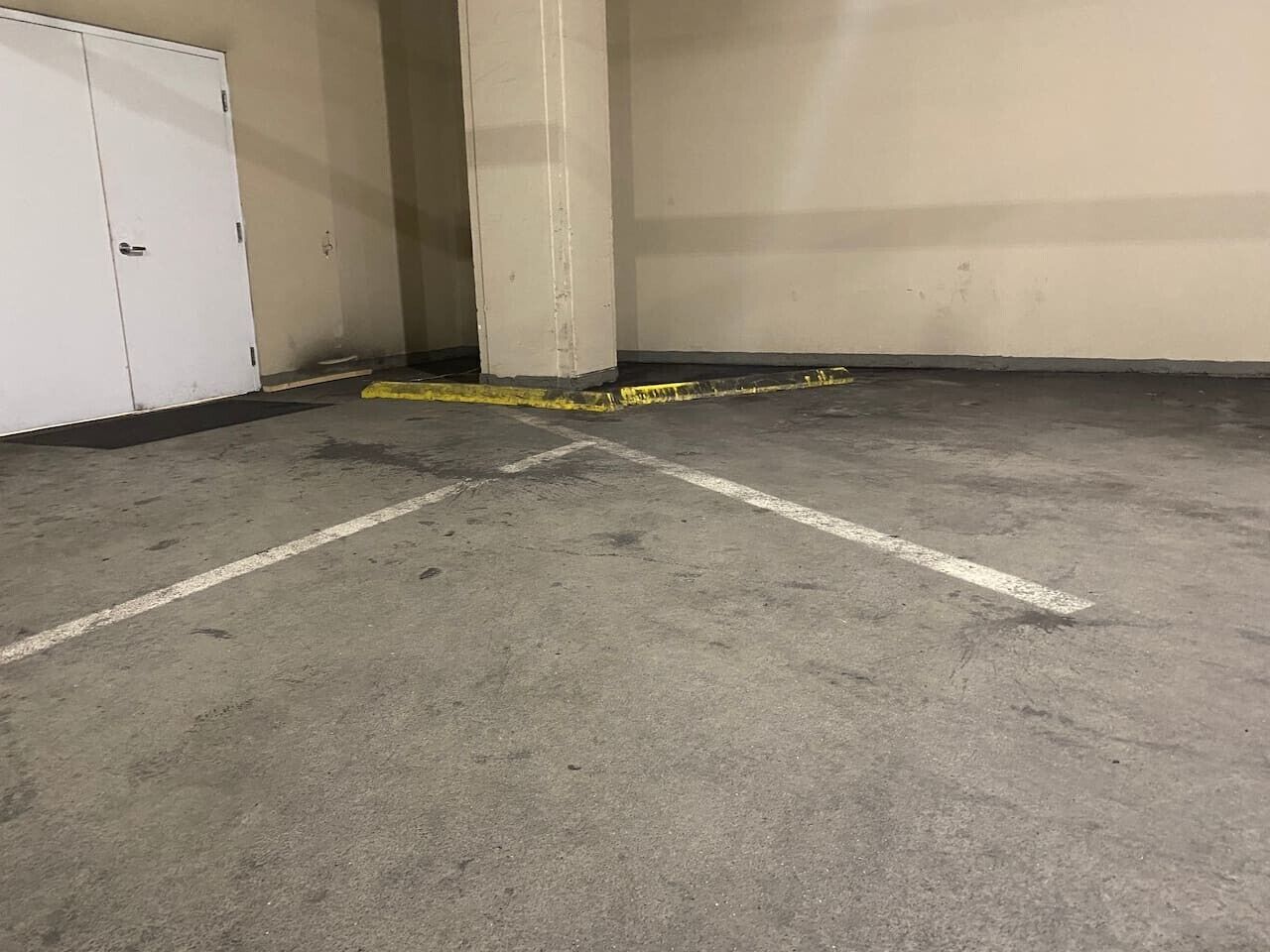 Autotalli, jossa on betonilattia, merkityt parkkipaikat ja valkoinen ovi.