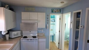 Una cocina compacta con electrodomésticos blancos, un microondas y una estufa. Hay un cartel en la pared que dice 'BEACH HOUSE'.