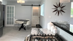 A modern kitchen with a gas stove, white cabinets, a marble countertop, and a dining area with a table and chairs. - Mid Century home close to beaches and downtown Dunedin. 1 block from the Trail. (Clearwater)