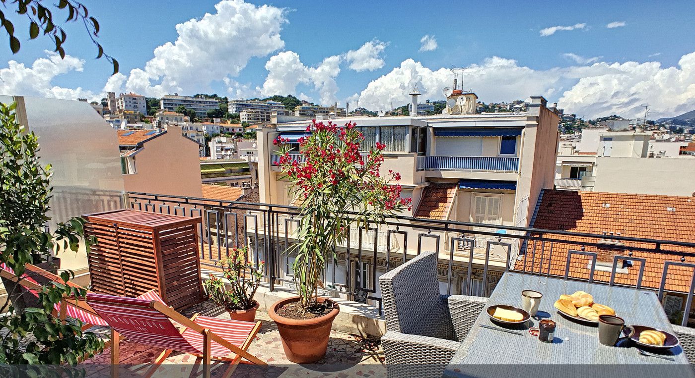 Une terrasse aménagée avec du mobilier d’extérieur, des plantes en pot et une table où sont disposés des plats, offrant une vue sur le paysage urbain.