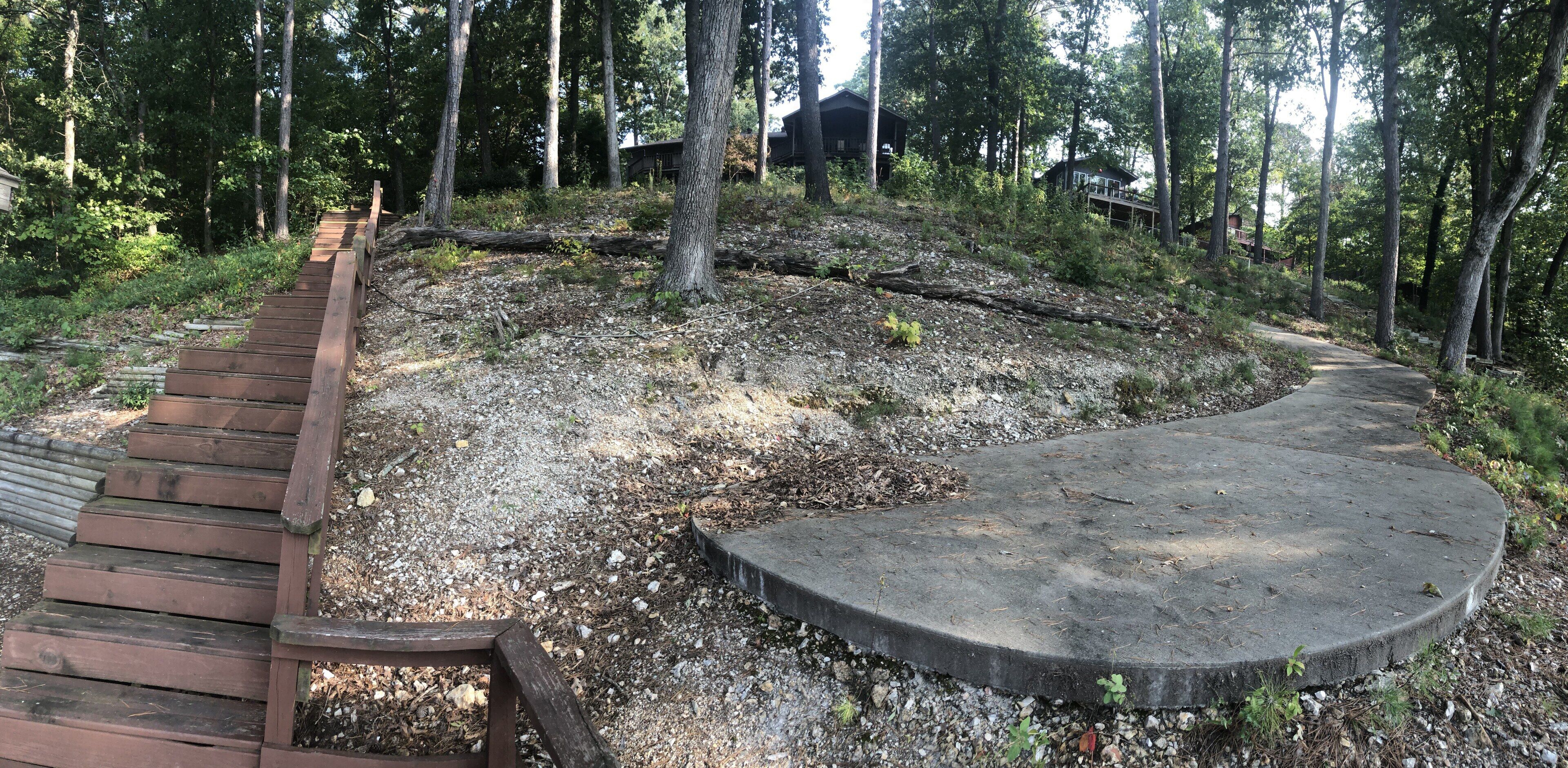 A wooden staircase leading up a gravel path surrounded by trees, with a concrete platform at the top.