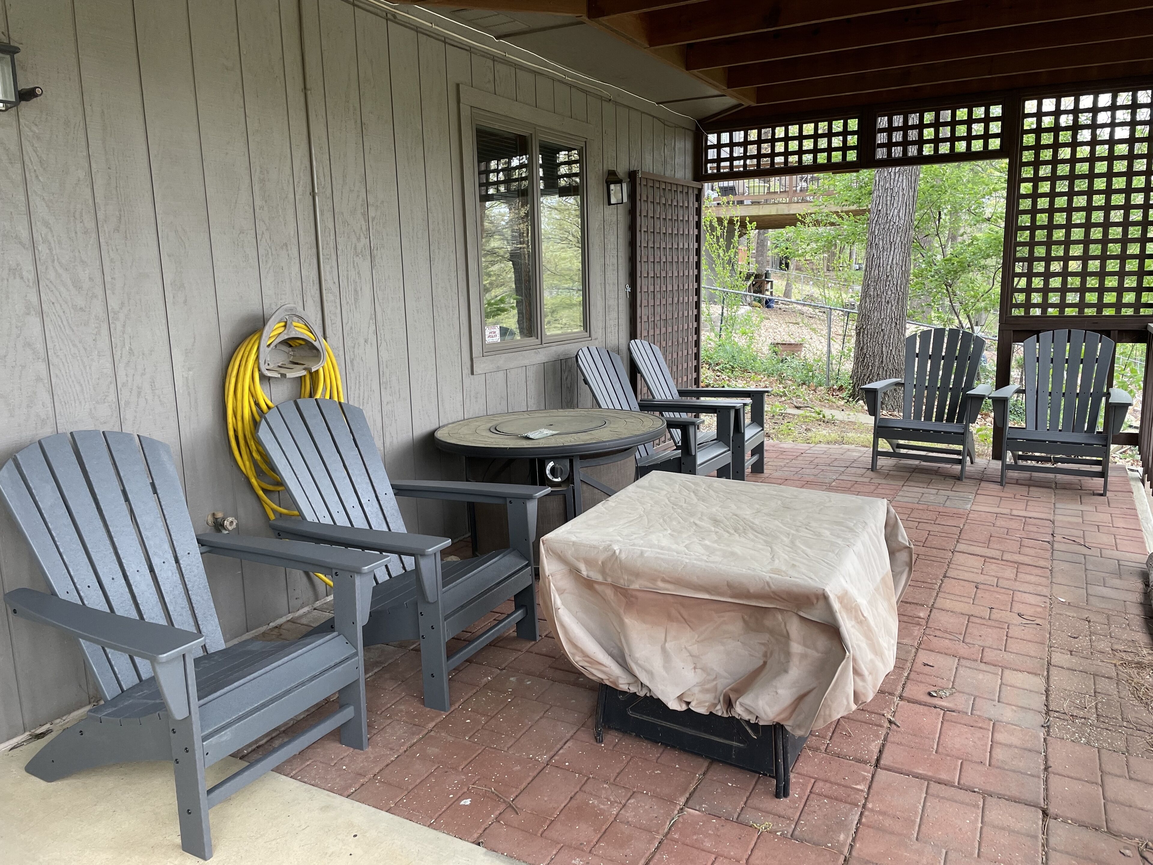 Une terrasse extérieure avec des fauteuils Adirondack, une table couverte et un tuyau d’arrosage.