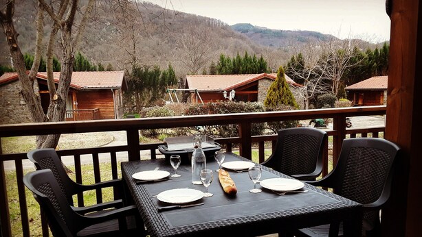 A table set for four on a wooden deck with a view of cabins and mountains. - Le Hameau du Comté de Foix (Mercus-Garrabet)