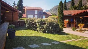 A courtyard with wooden buildings, a paved path, and a mountain backdrop. - Le Hameau du Comté de Foix (Mercus-Garrabet)