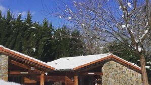 A lodge with a stone exterior and a wooden roof, surrounded by snow and trees. - Le Hameau du Comté de Foix (Mercus-Garrabet)