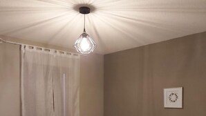 A bedroom with a bed, a hanging light fixture, a wall-mounted picture, and a curtain. - Le Hameau du Comté de Foix (Mercus-Garrabet)