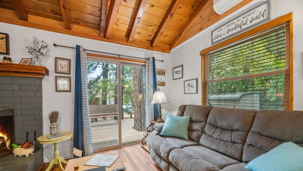 A cozy living room with a fireplace, a sofa, and a large window with blinds. - JUST FOR 2!  NEAR ENTERTAINMENT/RESTAURANTS - HOT TUB - FIRE PIT - BBQ & A/C (Big Bear Lake)