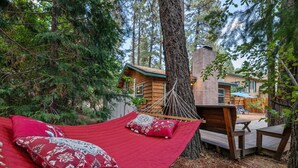 A hammock with red bedding and decorative pillows, set against a backdrop of tall trees and a wooden cabin. - JUST FOR 2!  NEAR ENTERTAINMENT/RESTAURANTS - HOT TUB - FIRE PIT - BBQ & A/C (Big Bear Lake)