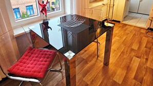 Un comedor moderno con una mesa de vidrio, una silla con cojín rojo y vistas a edificios.