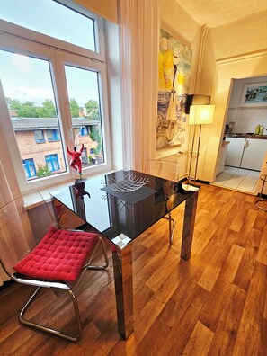 A modern dining area with a glass table, a red cushioned chair, and a view of buildings outside.