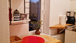 Una cocina compacta con armarios blancos, encimera de madera, tabla de cortar roja, cafetera y ventana con vistas al exterior.