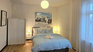 Un dormitorio con una cama, lámparas de noche, una lámpara de techo, un cuadro y un armario.
