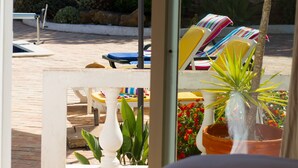 A view of a pool area with lounge chairs and umbrellas, a stone wall, and potted plants.